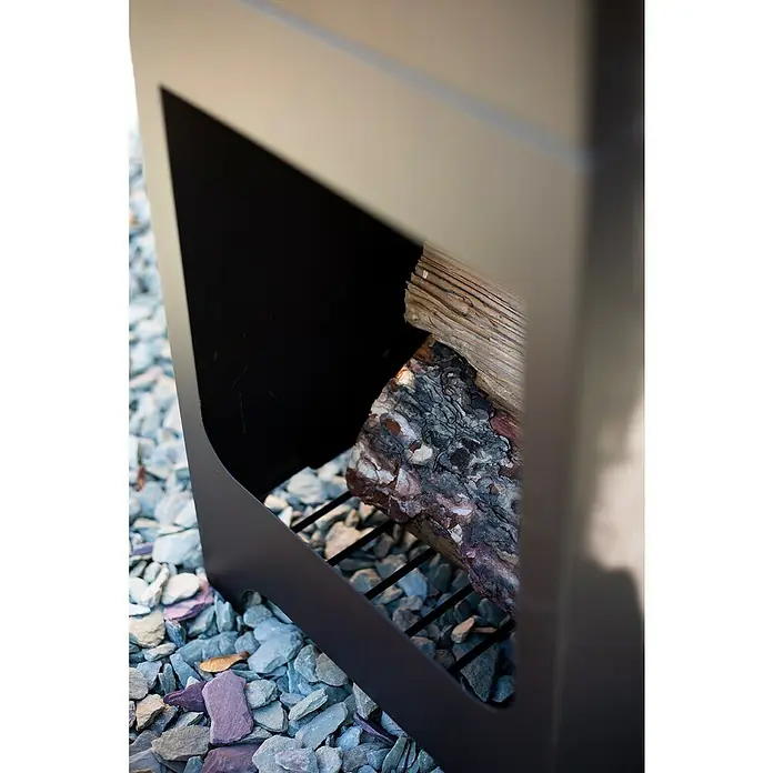 Buschbeck Chimenea para jardín Malmö - 36 x 36 x 150 cm, Acero, Recubrimiento en polvo - Primer plano de un moderno brasero de metal con troncos descansando sobre un lecho de grava, equipo para exteriores.