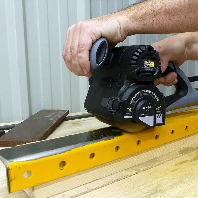 Fartools Renovierungsschleifer REX 80 Compact - 420 W - Nahaufnahme eines Far Tools REX 80 Werkzeugs beim Schneiden eines gelben Metallstücks, das auf einer Holzoberfläche liegt.