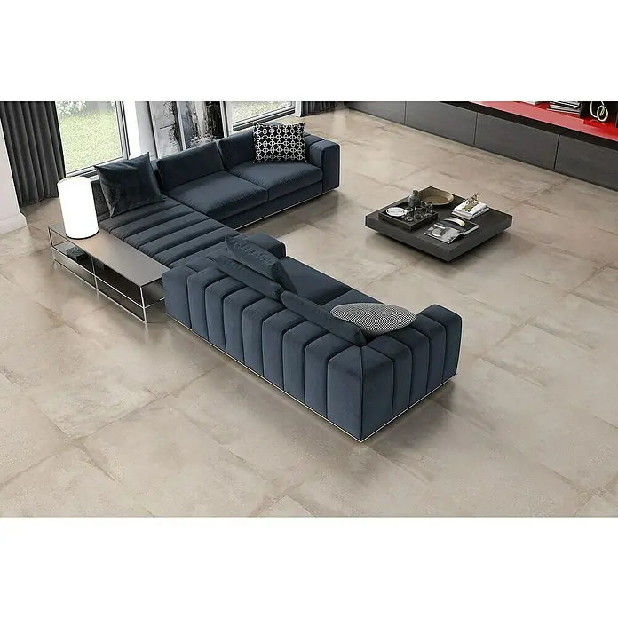 Pavimento porcelánico Origin - 60 x 120 cm, Arena, Mate, Rectificado - Elegante salón con sofá seccional modular en azul oscuro y una mesa de centro moderna sobre un piso de color claro.