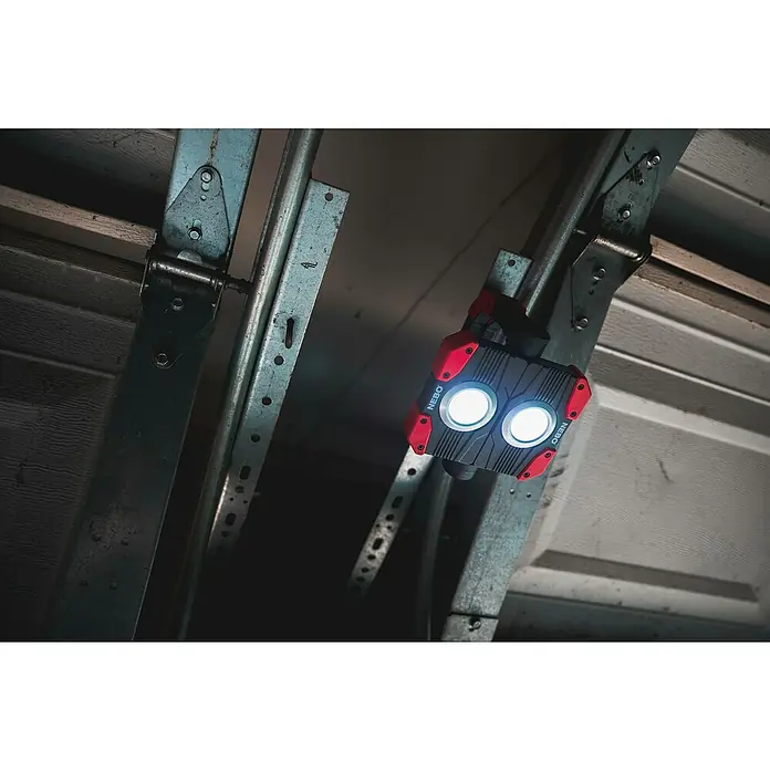 Nebo Tools Luz de trabajo LED Omini 2K - 2.000 lm - Primer plano de una luz de trabajo NEBO conectada a la estructura de una puerta de garaje, emitiendo luz brillante.