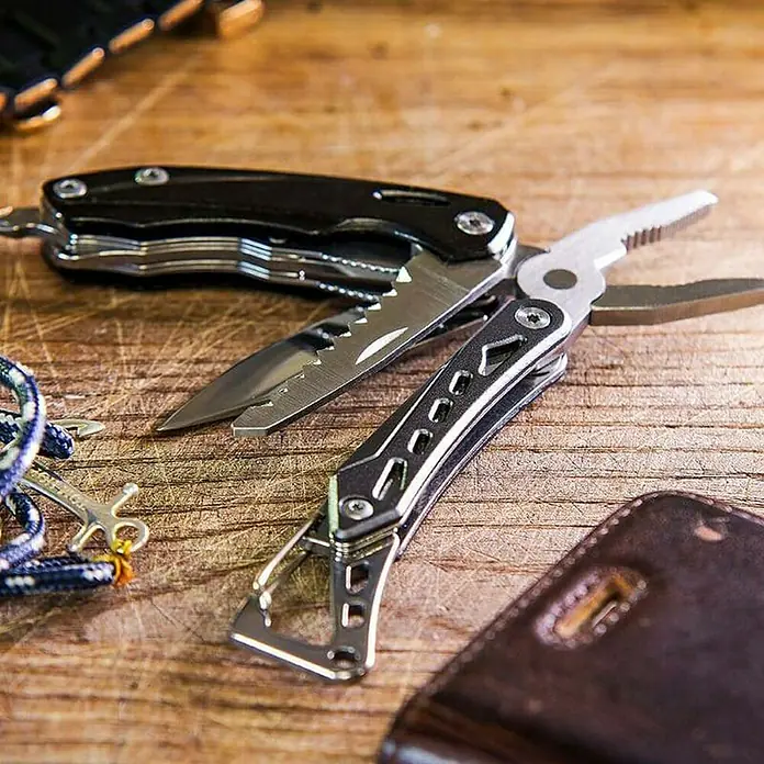Nebo Tools Set multiherramienta y linterna - Negro - Imagen de una multiherramienta con diversos implementos, incluyendo un cuchillo, alicates y destornilladores, sobre una mesa rústica de madera.
