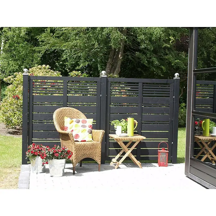 Plus Sichtschutzelement Silence - 120 x 170 cm, Holz, Schwarz - Einladende Gartenszene mit einem Rattansessel, einem Holztisch und dekorativen Akzenten vor einem stilvollen, schwarzen Holzzaun.