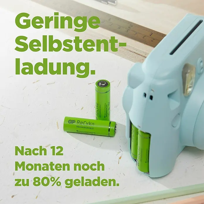 GP ReCyko Akku AA Mignon/HR6, 2100 mAh, NiMH, Ready-to-use 8Stk - 2.100 mAh - Das Bild zeigt GP ReCyko Akkus mit geringer Selbstentladung, die nach 12 Monaten noch zu 80% geladen sind, neben einer Kamera.