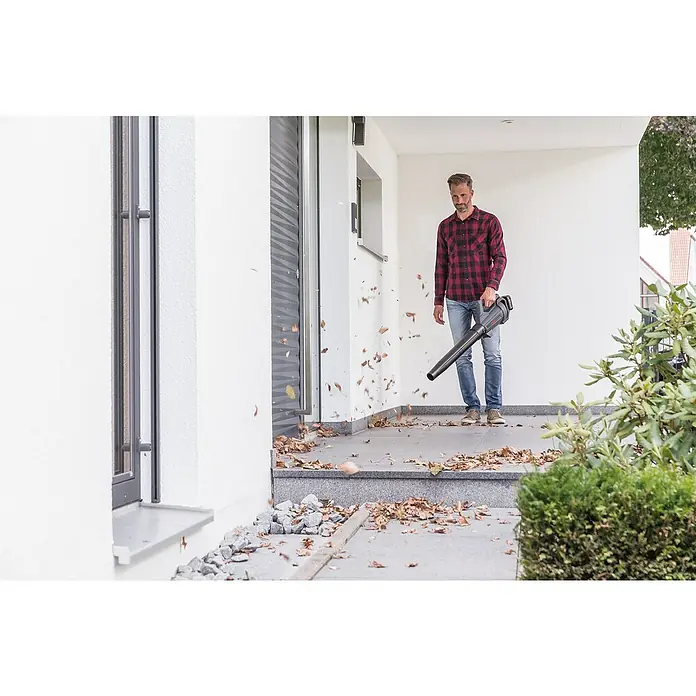 AL-KO Bosch Home & Garden Compatible Akku-Laubbläser LB 1860 SET - 18 V, 1 Akku, 2,5 Ah, Blasgeschwindigkeit: 165 km/h, Blasleistung: 450 m³/min - Ein Mann benutzt einen Laubbläser, um Blätter von einer Veranda zu entfernen. Das Laubblasgerät ist das Hauptprodukt im Bild.