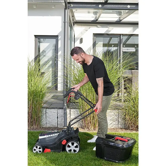 AL-KO Bosch Home & Garden Compatible Akku-Rasenmäher 3.82 Li Easy - 18 V, 2 Akkus, 4 Ah, Schnittbreite: 38 cm - Ein Mann montiert einen Rasenmäher im Garten. Der Rasenmäher ist schwarz und rot mit einem Fangkorb.