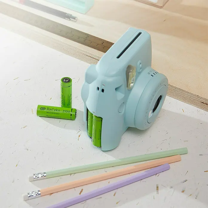 GP ReCyko Akku AA Mignon/HR6, 2100 mAh, NiMH, Ready-to-use 8Stk - 2.100 mAh - Hellblaue Sofortbildkamera mit Batterien und Stiften auf einem Tisch. Ideal für kreative Projekte und zum Festhalten besonderer Momente.