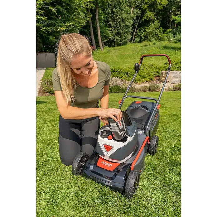 AL-KO 36V Akku-Rasenmäher 42.2 Li - 36 V, 1 Akku, 4 Ah, Schnittbreite: 42 cm - Eine blonde Frau kniet neben einem AL-KO Rasenmäher und setzt einen Akku ein, um ihn für die Gartenarbeit vorzubereiten.