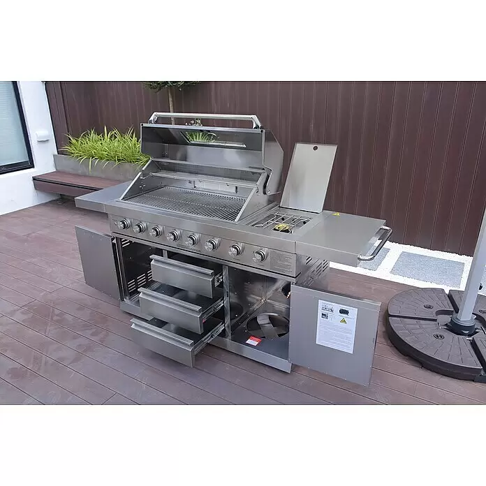 Buschbeck Outdoorküche Bristol - Edelstahl, Silber, Material Grillfläche: Edelstahl, Anzahl Brenner: 6 Stk. - Großer Edelstahl-Gasgrill mit Seitenbrenner und Schubladen auf einer Holzterrasse.