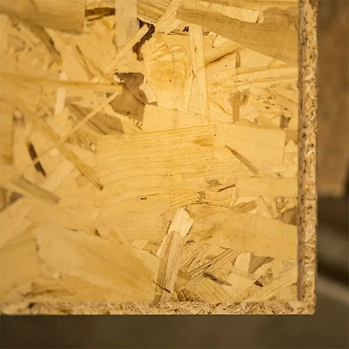 Tablero de OSB machihembrado - 250 cm x 67,5 cm x 16 mm - Primer plano de un tablero OSB que muestra la textura y la composición de la madera de ingeniería. El tablero se compone de hebras de madera prensada y adhesivo.