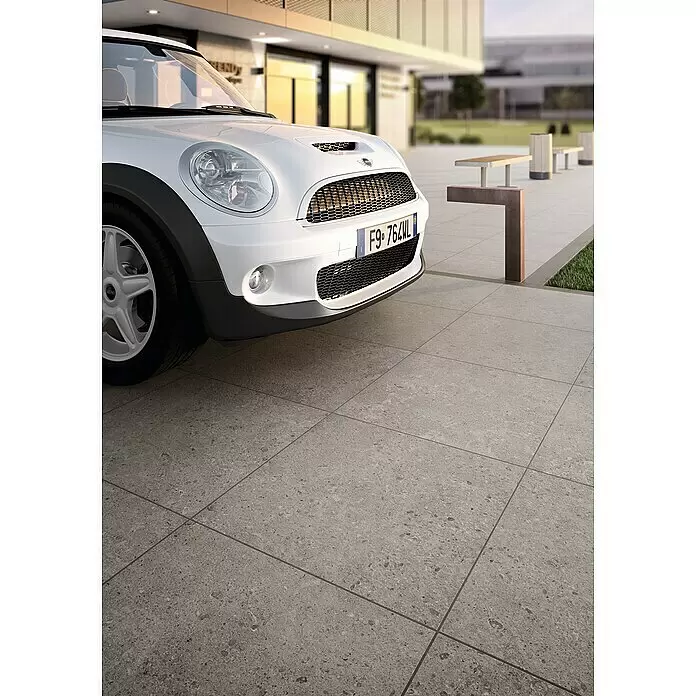 Marazzi Terrassenfliese Esterno 20T Gris Fleury - 60 x 60 x 2 cm, Grau, Matt - Graue, texturierte Outdoor-Pflastersteine, auf denen ein weißes Auto in urbaner Umgebung parkt.
