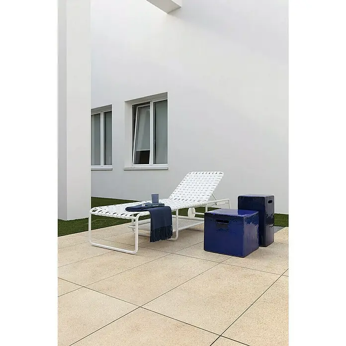 Marazzi Terrassenfliese Esterno 20T Jerusalem Avori50 x 100 x 2 cm, Hellbeige, Matt - Eine weiße Sonnenliege mit blauen Hockern auf einer Terrasse. Die Liege ist mit einem blauen Tuch und einem Buch dekoriert.