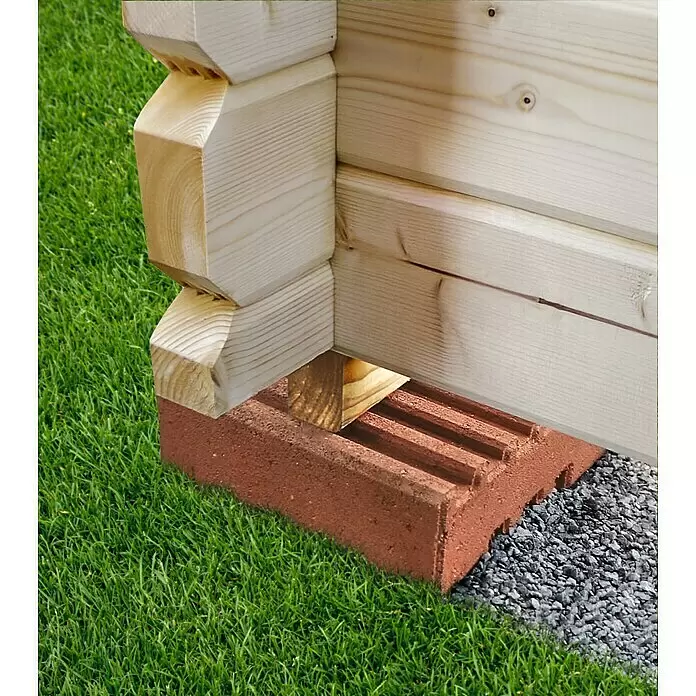 Christoph Fundamentstein - 22 x 22 x 8 cm, Beton - Rötlich-brauner Fundamentstein stützt die Ecke einer hellen Holzblockhütte auf Kies.