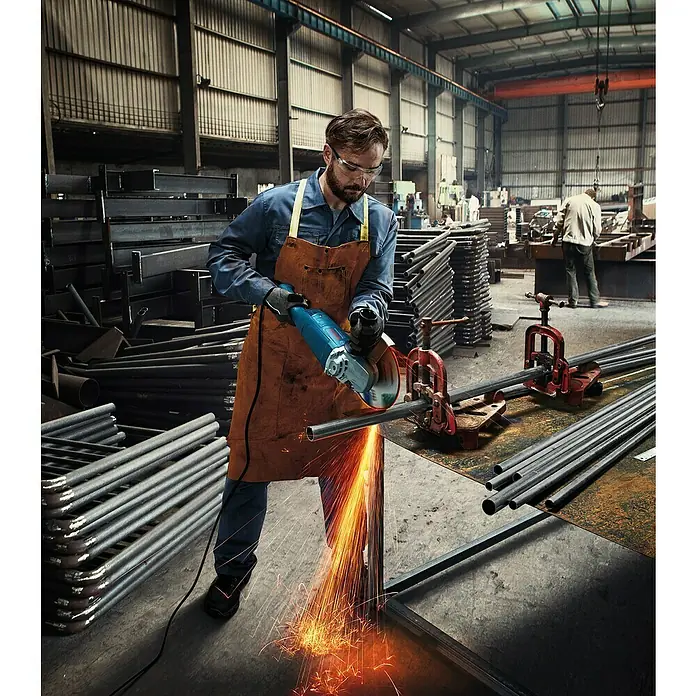 Bosch Professional Amoladora angular eléctrica GWS 20-230 J - 2.000 W, Diámetro disco: 230 mm, Número de revoluciones de marcha en vacío: 6.500 r.p.m. - Trabajador usando una amoladora angular para cortar tubos metálicos en una fábrica. Chispas volando, equipo de protección puesto.