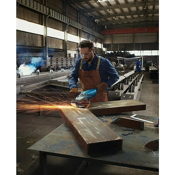 Bosch Professional Amoladora angular eléctrica GWS 20-230 J - 2.000 W, Diámetro disco: 230 mm, Número de revoluciones de marcha en vacío: 6.500 r.p.m. - Un trabajador usa una amoladora angular Bosch en un taller, saltan chispas mientras esmerila metal.