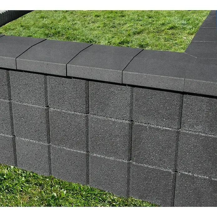 Christoph Mauerabdeckplatte R - 25 x 26 x 4,8 cm, Anthrazit, Beton - Naheaufnahme einer stabilen, grauen Gartenmauer aus Betonsteinen, die ein Blumenbeet oder eine Terrasse stilvoll begrenzt.