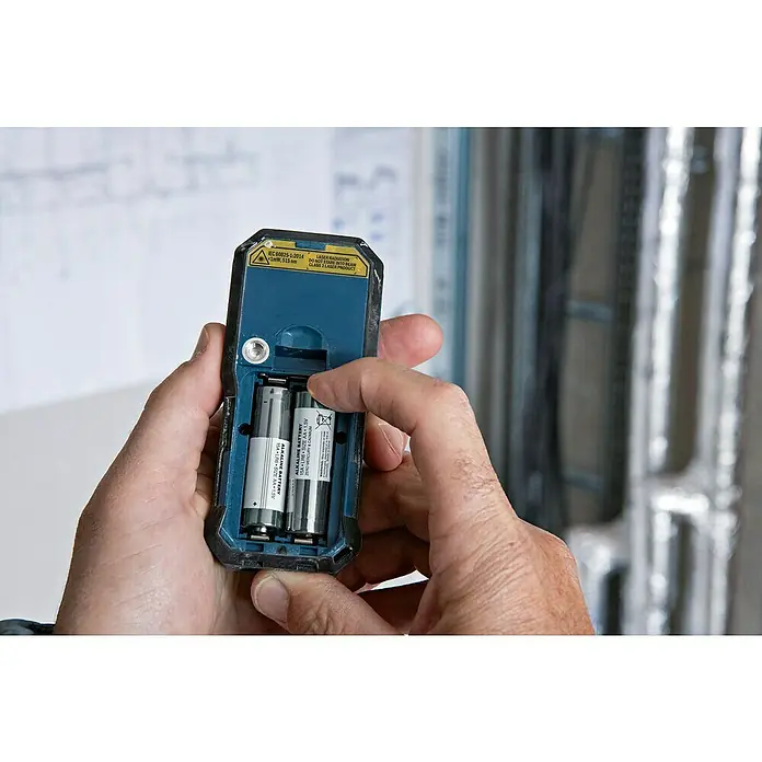 Bosch Professional Laserentfernungsmesser GLM 50-25 G - Messbereich: 0,05 - 50 m - Nahaufnahme eines Händepaares, das Batterien in ein blaues Bosch-Messgerät einlegt.