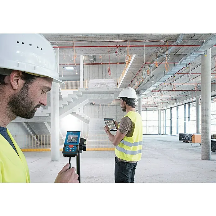 Bosch Professional Laserentfernungsmesser GLM 100-25 C - Messbereich: 0,08 - 100 m - Zwei Bauarbeiter mit Schutzhelmen und Westen, die einen Bosch-Laser-Entfernungsmesser und ein Tablet auf einer Baustelle verwenden.