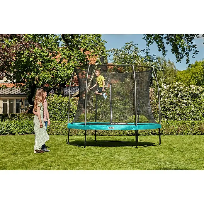 Salta Trampolin Comfort Edition - Durchmesser: 251 cm, Grün - Ein Junge springt auf einem Salta-Gartentrampolin mit Sicherheitsnetz, während zwei Personen zusehen. Das Trampolin steht auf einer grünen Wiese.