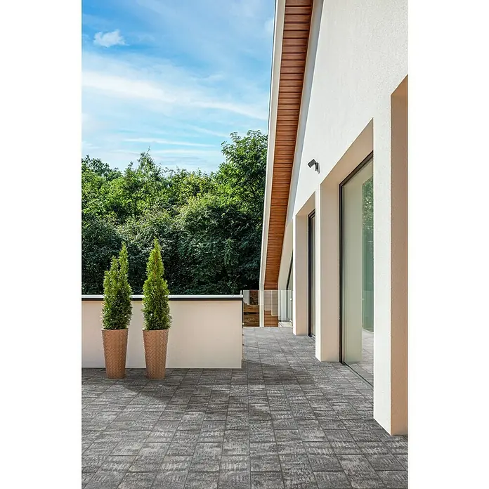 Terrassenplatte Latina - 48 x 24 x 3 cm, Grau/Schwarz, Beton - Außenaufnahme einer Terrasse mit stilvollen grauen Pflastersteinen, dekoriert mit zwei schlanken, grünen Zypressen in Terrakotta-Töpfen.