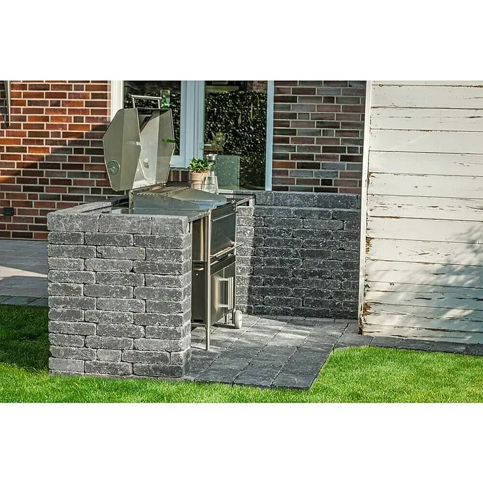Diephaus Mauerstein Austin - 30 x 20 x 10 cm, Basalt, Beton - Einbaugrill mit Steinumrandung im Außenbereich, integriert in eine gepflasterte Fläche neben einer Holzwand und einem Rasen.