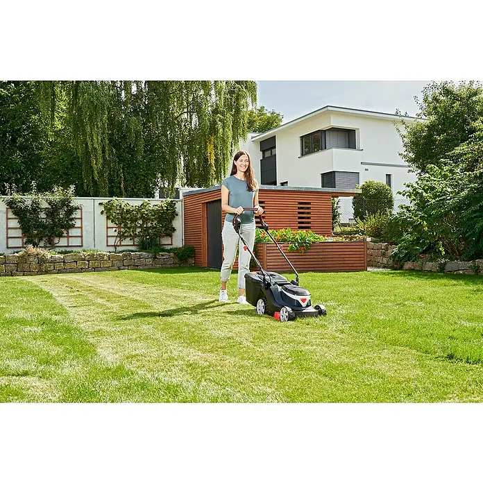 AL-KO Easy Elektro-Rasenmäher - 1.600 W, Schnittbreite: 38 cm - Eine Frau mäht mit einem Rasenmäher den Rasen im Garten, ein modernes Haus im Hintergrund.
