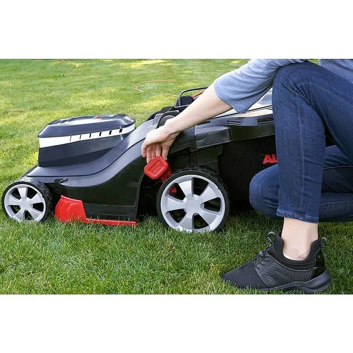 AL-KO Comfort Elektro-Rasenmäher - 1.600 W, Schnittbreite: 38 cm - Nahaufnahme eines AL-KO Rasenmähers auf Rasen, bei dem eine Person die Schnitthöhe mit einem roten Knopf einstellt.