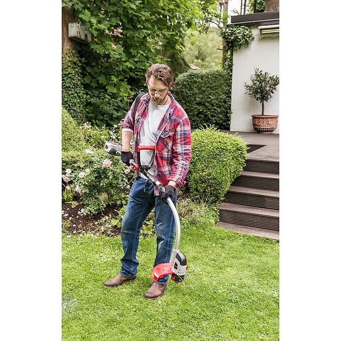 AL-KO 36V Rasentrimmeraufsatz GTA 430 - Passend für: Multitool MT 40 Li/MT 36 Li - Ein Mann im Garten bedient einen Rasentrimmer, um den Rasen zu pflegen, wobei er Schutzkleidung trägt.