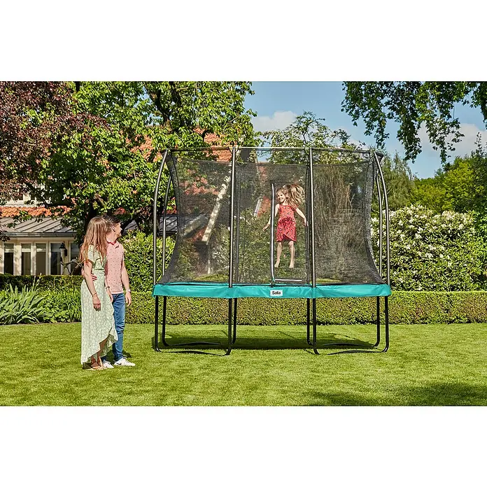 Salta Trampolin Comfort Edition - Grün, L x B: 244 x 366 cm - Ein grünes Salta-Trampolin mit Sicherheitsnetz im Garten, während ein Mädchen springt und zwei Kinder zusehen.