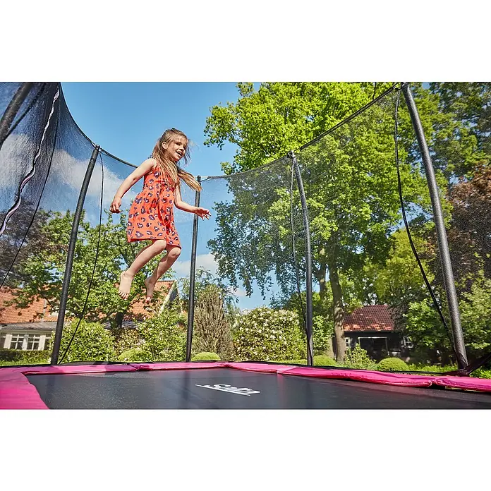 Salta Trampolin Comfort Edition - Pink, L x B: 214 x 305 cm - Ein junges Mädchen springt auf einem Salta-Trampolin mit Sicherheitsnetz vor üppigem Grün. Das Trampolin hat einen pinkfarbenen Rand.