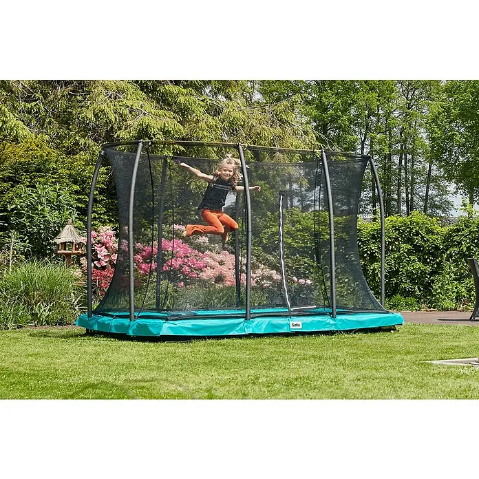 Salta Trampolin Comfort Edition Ground - Grün, L x B: 244 x 366 cm - Kind springt auf einem Salta Gartentrampolin mit Sicherheitsnetz, umgeben von üppigem Grün und Blumen.