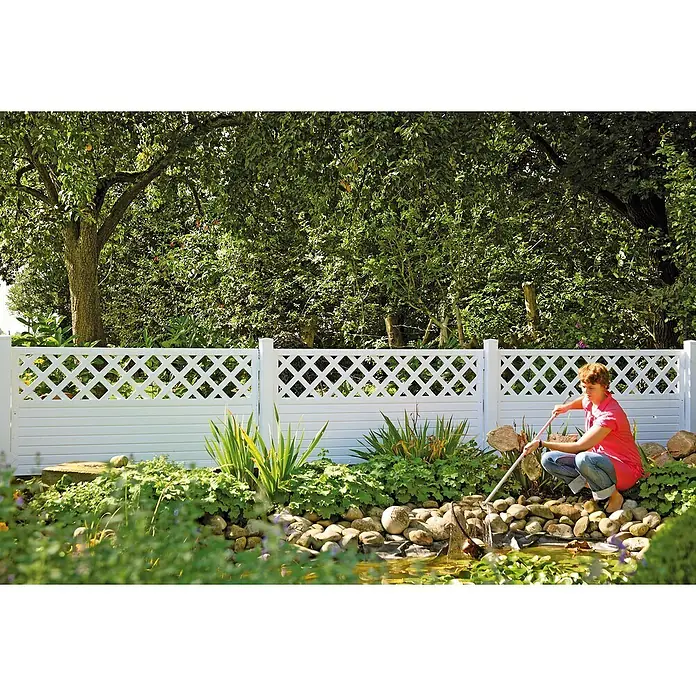 T & J Lightline Sichtschutzelement Rankgitter - 180 x 90 cm, Mit Rankgitter, Weiß - Eine Frau reinigt mit einem Stock einen Teich, der mit einer weißen, dekorativen Gartenumzäunung umgeben ist.