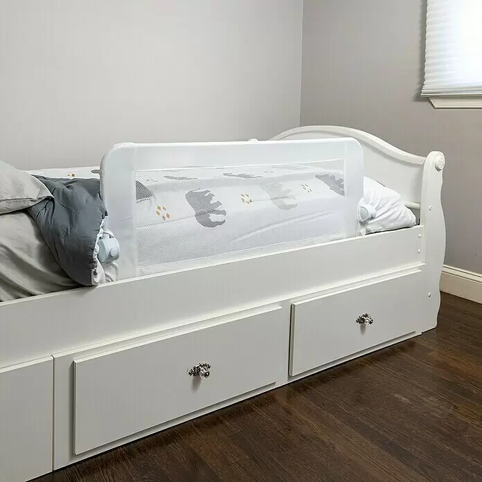 Dreambaby Bettgitter Bett Maggie - Weiß - Weißes Netzbettgitter an einem Kinderbett mit gemusterter Bettwäsche als Sicherheitsbarriere befestigt.