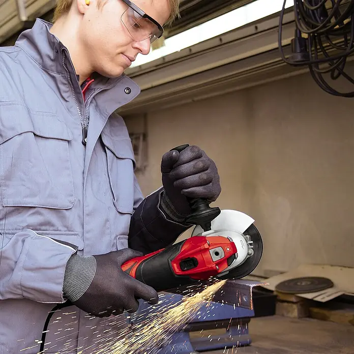 Einhell Expert Elektro-Winkelschleifer TE-AG 125/750 - Durchmesser Scheibe: 125 mm, Leerlaufdrehzahl: 12.000 U/min - Ein Arbeiter benutzt einen roten Winkelschleifer mit Funkenflug. Persönliche Schutzausrüstung wird getragen.