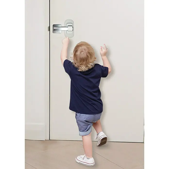 Dreambaby Türsicherung Türklinke - 1 Stk., Weiß - Kind versucht, eine Tür mit einem Türgriff und einer Kindersicherung zu öffnen, um die Sicherheit zu gewährleisten.