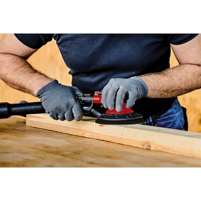 Einhell Haftschleifscheiben-Set - Durchmesser: 150 mm, Körnung: 40 - 120, 5 -tlg. - Ein Mann schleift ein Stück Holz mit einem Exzenterschleifer, er trägt dabei Handschuhe. Der Schleifer ist rot und schwarz.