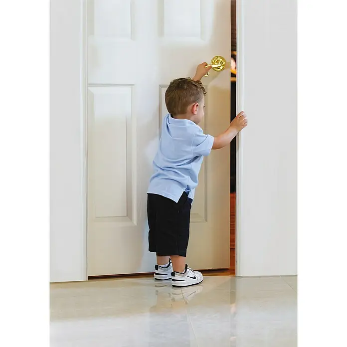 Dreambaby Türstopper - Weiß - Ein kleiner Junge in blauer Kleidung öffnet eine weiße Tür mit einem goldenen Türknauf. Er trägt lässige Shorts und bequeme Schuhe.