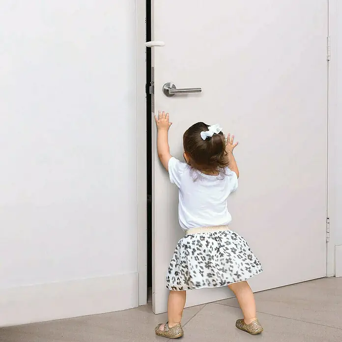 Dreambaby Türstopper Silikon - Weiß - Kind, das versucht, eine Tür mit einem installierten Türstopper zu öffnen. Der Türstopper verhindert versehentliches Zuschlagen.