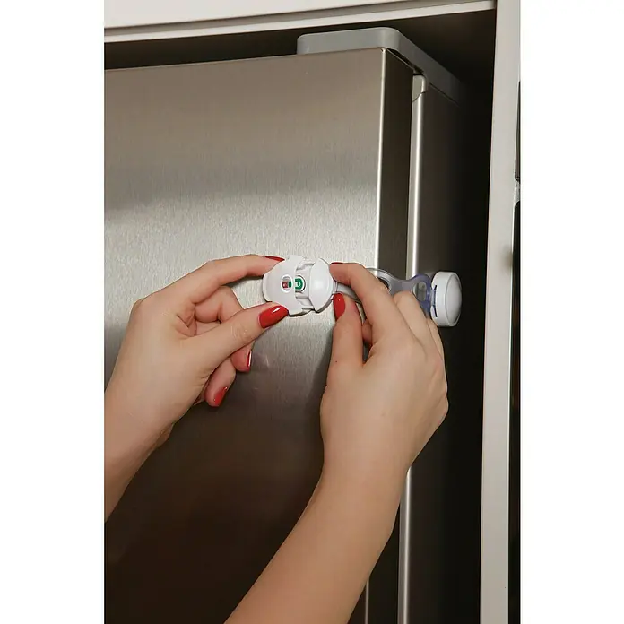 Dreambaby Multifunktionsverschluss EZY-Check - Farbe: Weiß - Eine Person befestigt ein weißes Schrankschloss an einem Kühlschrank, um ihn kindersicher zu machen. Das Schloss ist aus Kunststoff und hat einen Drehmechanismus.