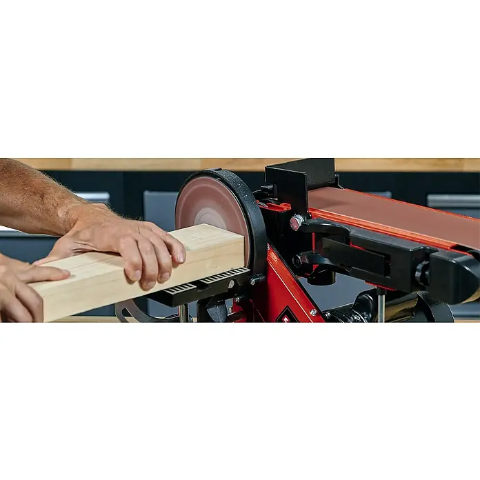 Einhell Schleifscheiben - Durchmesser: 150 mm, Körnung: 80, Passend für: Einhell Stand-Band-Tellerschleifer TC-US 400 & TC-US 380, 3 Stk. - Ein Mann benutzt eine Bandschleifmaschine, um ein Stück Holz zu bearbeiten. Das Gerät ist rot und schwarz und steht auf einer Werkbank.