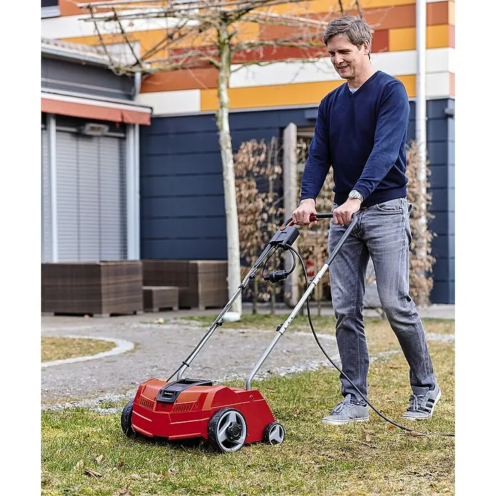 Einhell Classic Elektro-Vertikutierer GC-ES 1231/1 - 1.200 W, Arbeitsbreite: 31 cm - Ein Mann benutzt einen roten Einhell Elektro-Vertikutierer im Garten, um den Rasen zu pflegen. Ideal für kleine bis mittelgroße Rasenflächen.