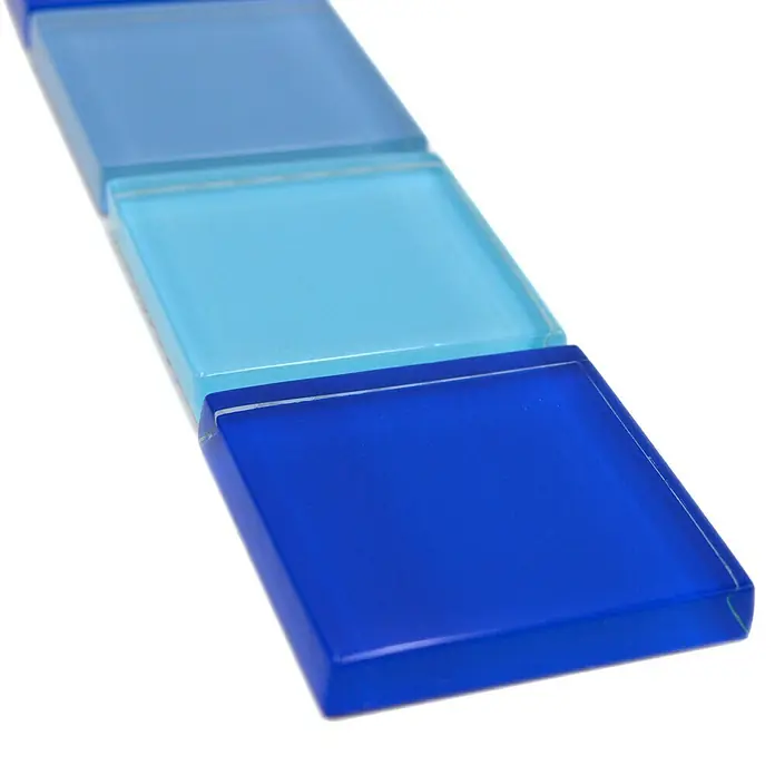Fliesenbordüre Vision BO NB19480 - 4,8 x 30 cm, Blau, Glänzend - Nahaufnahme von drei quadratischen Glasfliesen in verschiedenen Blautönen, die ein stilvolles und modernes Designelement darstellen.