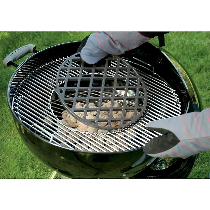Weber Gourmet BBQ System Grillrost Sear Grate - L x B: 30 x 30 cm, Durchmesser: 30 cm, Gusseisen - Grillvorbereitung: Hände mit Handschuhen platzieren einen Holzkohleeinsatz über Holzkohlebriketts in einem schwarzen Kugelgrill im Freien.