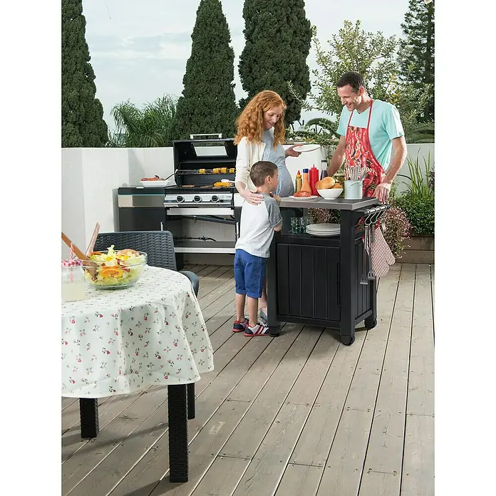 Keter Mesa auxiliar de jardín Unity - L x An: 82 x 52 cm, Marrón - Una familia disfruta de una barbacoa al aire libre con un práctico carro de barbacoa, que sirve como espacio de trabajo y para el almacenamiento.