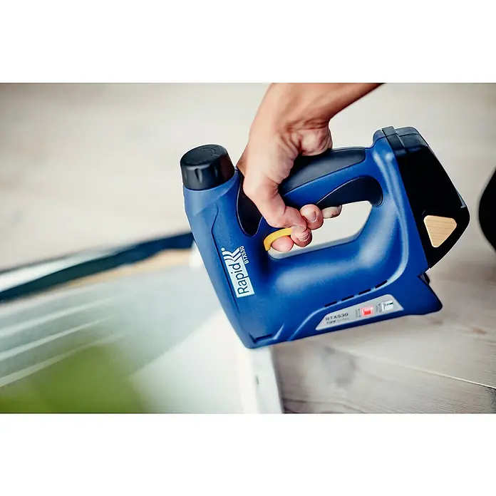 Rapid Akku-Tacker BTX530 - 7,2 V, Li-Ionen, 1,3 Ah, 1 Akku, Klammertiefe: 6 mm - 14 mm - Nahaufnahme eines blauen Rapid BTX530 Akku-Tackers, der von einer Hand gehalten wird. Ideal für Befestigungen bei Polsterarbeiten oder Dekorationen.