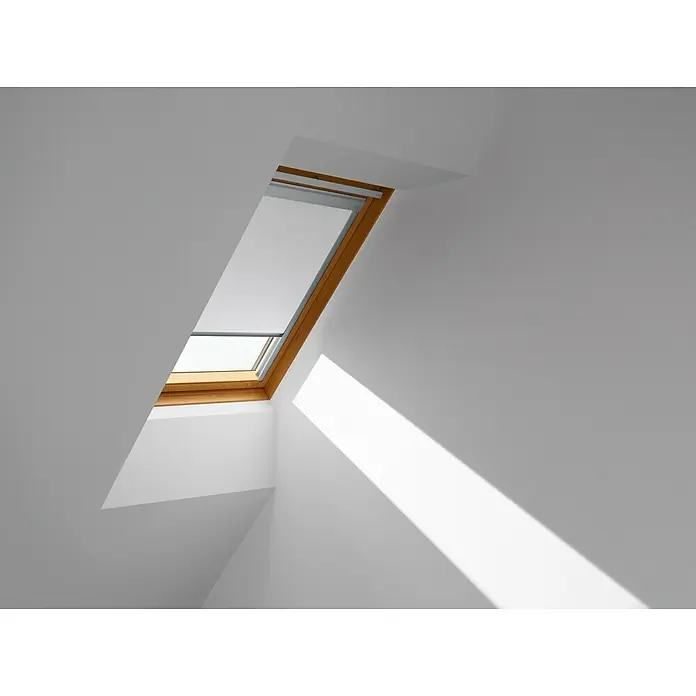 Velux Dachfensterrollo Classic DBL U04 4288 - Farbe: Weiß - 4288, Farbe Schiene: Aluminium, Manuell - Nahaufnahme eines Dachfensters mit Holzrahmen in einem hellen Raum, das einen Lichtstrahl auf die weiße Wand wirft. Das Fenster lässt Tageslicht herein.