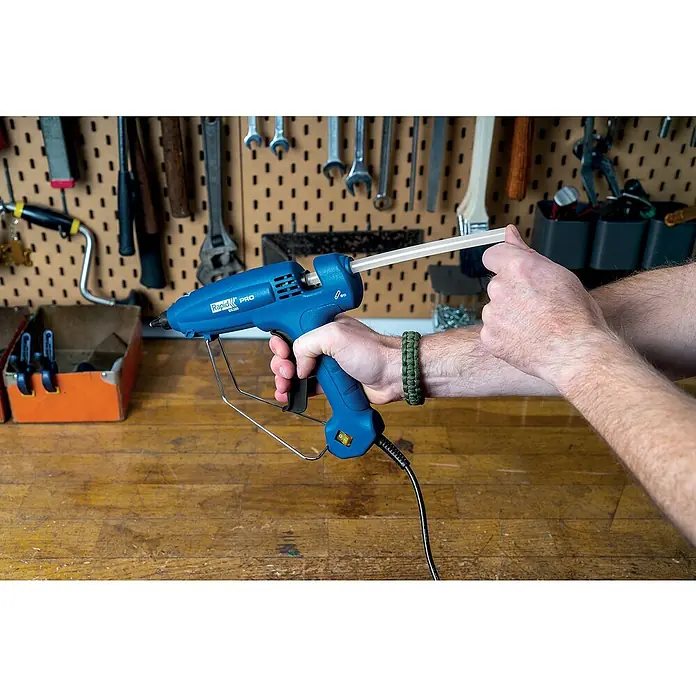 Rapid Heißklebepistole EG 320 PRO - Durchmesser Klebepatrone: 12 mm, 195 °C, 180 W - Nahaufnahme einer blauen Rapid PRO EC320 Heißklebepistole mit einer Hand, die einen Klebestift hineinschiebt, vor einer Werkzeugwand.