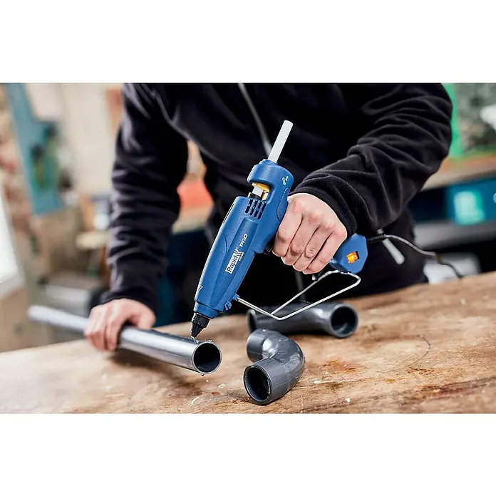 Rapid Heißklebepistole EG 320 PRO - Durchmesser Klebepatrone: 12 mm, 195 °C, 180 W - Nahaufnahme einer Rapid PRO EG330 Heißklebepistole im Einsatz, die auf einem Holztisch Metallrohre verklebt.