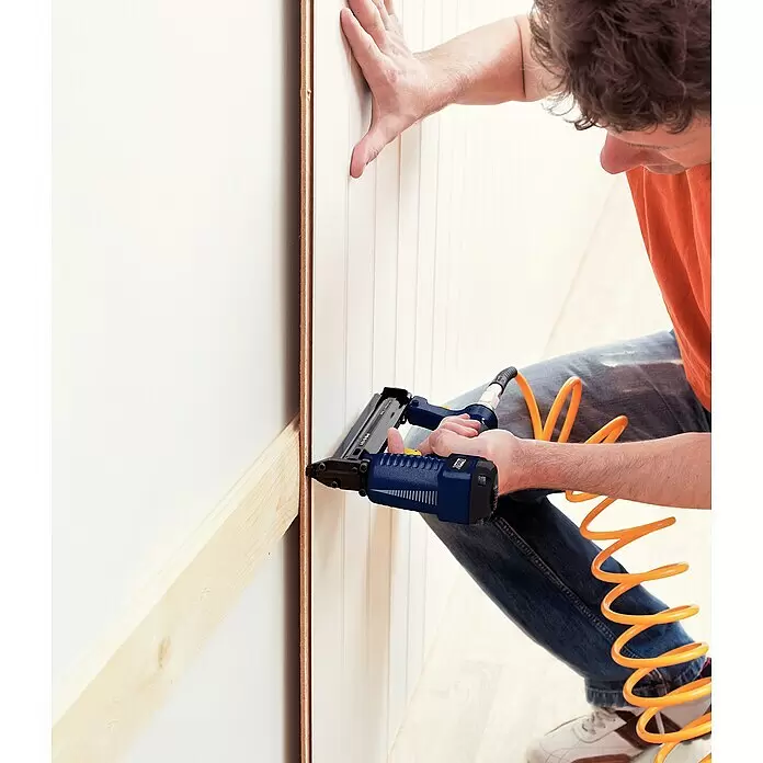 Rapid Clavadora combinada AirTac PBS121 - Profundidad de grapado: 12 mm - 30 mm, Apto para: Grapas tipo 606, Neumático - Pistola de clavos azul y negra utilizada por una persona para fijar paneles de madera a una pared.