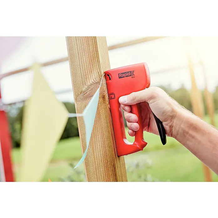 Rapid Handtacker R53E - Klammertiefe: 4 mm - 10 mm, Geeignet für: Klammern Typ 53 - Nahaufnahme eines roten Rapid R53 Tacker, der an einem Holzpfosten befestigt ist, um eine bunte Partygirlande zu befestigen.