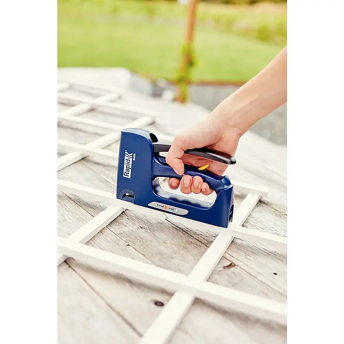 Rapid Kombi-Handtacker R453E - Klammertiefe: 6 mm - 14 mm, Geeignet für: Klammern Typ 53 - Das Bild zeigt einen blauen Rapid R453 Tacker beim Heften eines weißen Holzrahmens, bedient von einer Hand. Fokus auf Präzision.